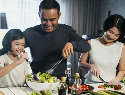 Un couple et leur fille préparent une salade à la maison.