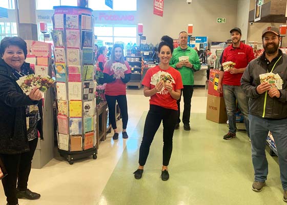 Un groupe d’employés et de clients de Foodland qui tiennent des cartes-cadeaux en respectant la distanciation physique.