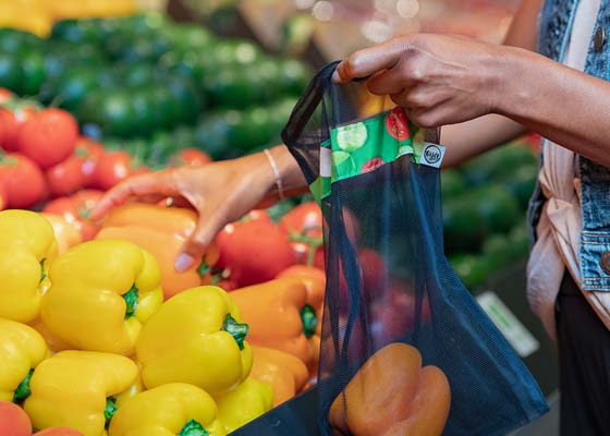 Une personne met des poivrons orange dans un sac réutilisable à l’épicerie.