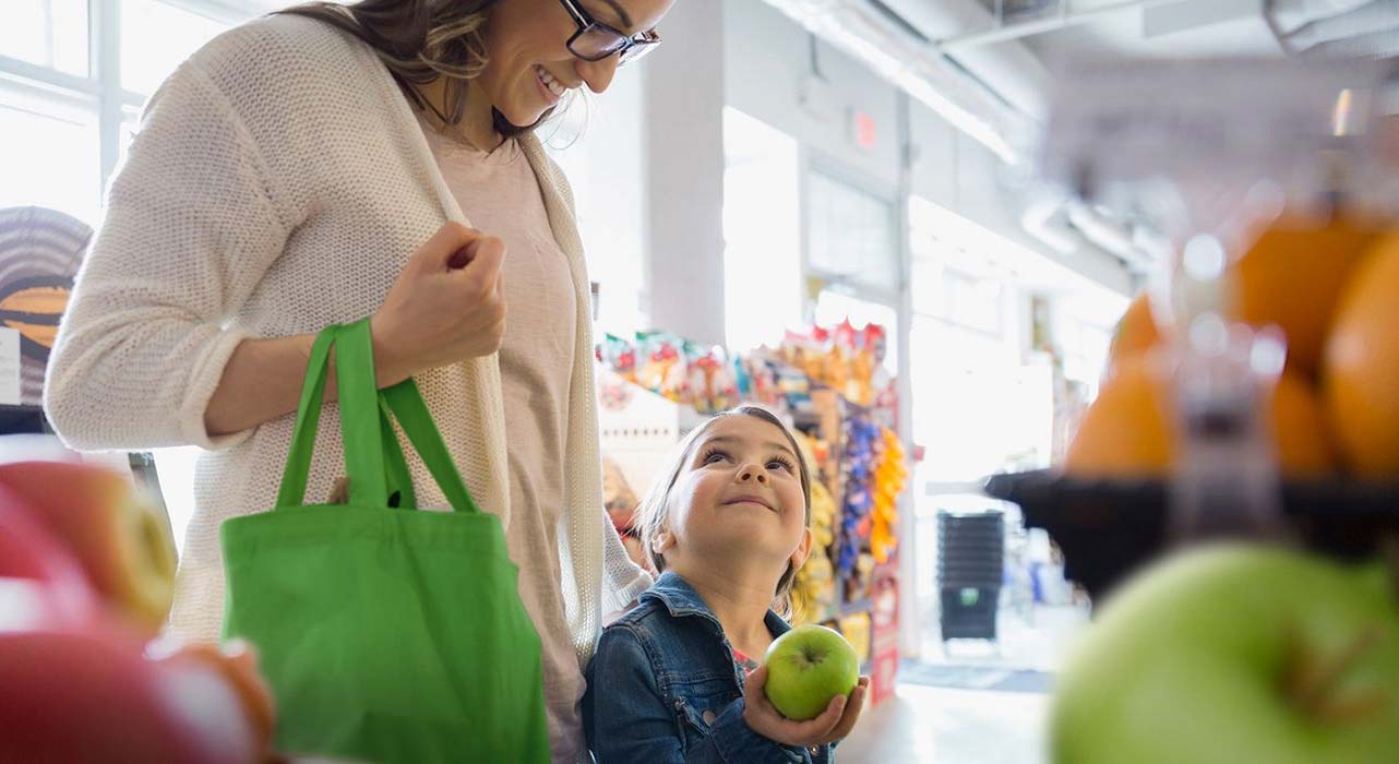 Une petite fille tient une pomme et regarde sa mère à l’épicerie