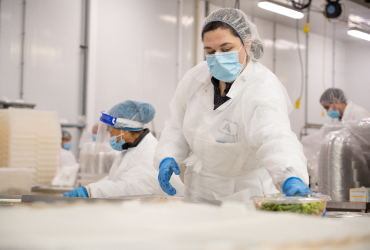 Workers in protective clothing and face masks handle food containers in a sterile processing environment.