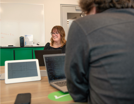 In this image, a woman discusses something with the team and laughs.